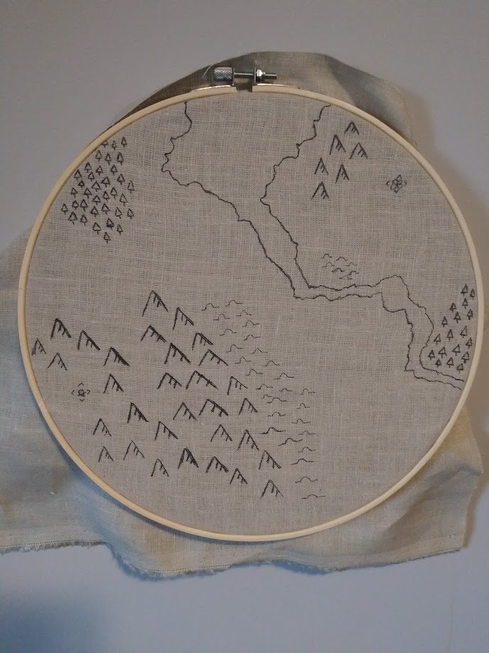 The map for Something Wild. It is a plain cream linen map with handdrawn depictions of rivers, mountains, and forests. It is stretched over a 12" hoop. 